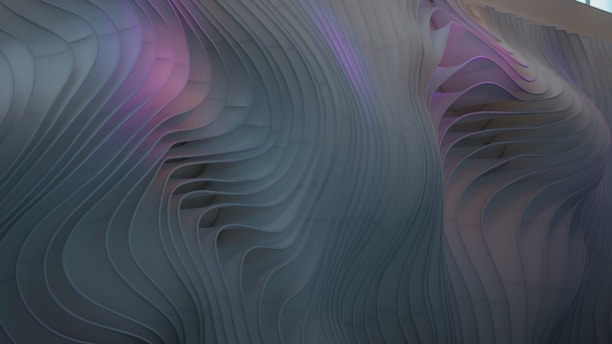 The image showcases a wavy, textured surface with flowing, organic lines and grooves. The surface has a three-dimensional appearance with gentle curves that create a sense of movement. A subtle blend of colors, including shades of purple and grey, adds depth to the abstract design.