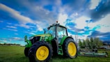 Tractor with attachments parked beside tropical plants under a bright sky.