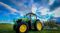 A tractor parked beside freshly tilled soil under a bright blue sky.