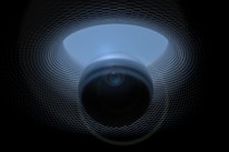 A surreal digital artwork featuring a spherical object positioned centrally, surrounded by a patterned, tunnel-like structure. The texture of the tunnel resembles a grid or mesh, creating a sense of depth and movement. Lighting effects enhance the mysterious and futuristic atmosphere.