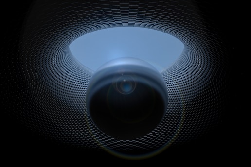 A surreal digital artwork featuring a spherical object positioned centrally, surrounded by a patterned, tunnel-like structure. The texture of the tunnel resembles a grid or mesh, creating a sense of depth and movement. Lighting effects enhance the mysterious and futuristic atmosphere.