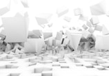 A collection of three-dimensional geometric shapes, primarily cubes and rectangular prisms, appears to be floating and tumbling in a white, minimalistic environment. The arrangement creates a sense of chaos and movement.