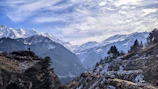 A panoramic view of snow-capped Himalayan mountains with expedition vehicles parked nearby.
