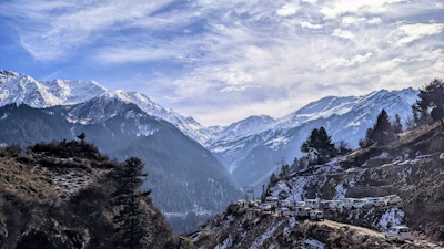 A panoramic view of snow-capped Himalayan mountains with expedition vehicles parked nearby.