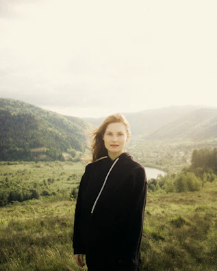 Close-up of a woman wearing a witty rovance hoodie, smiling against a backdrop of rolling hills