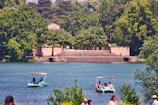 Families laughing and riding pedalos near the water's edge surrounded by lush greenery.