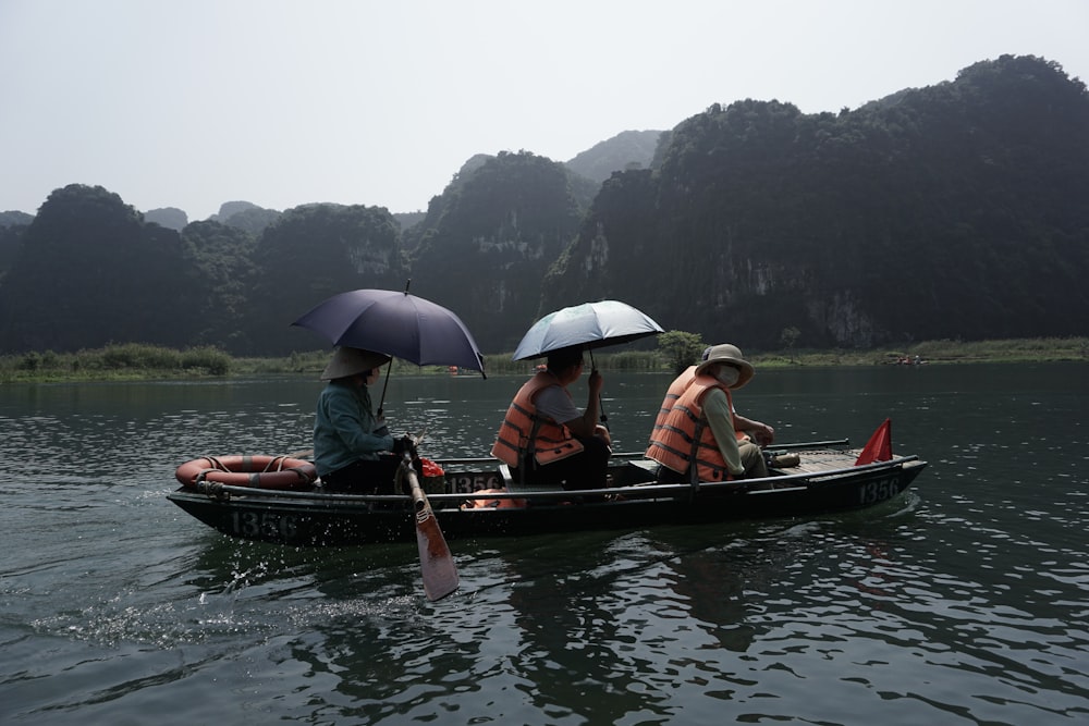 three people in a small boat with umbrellas