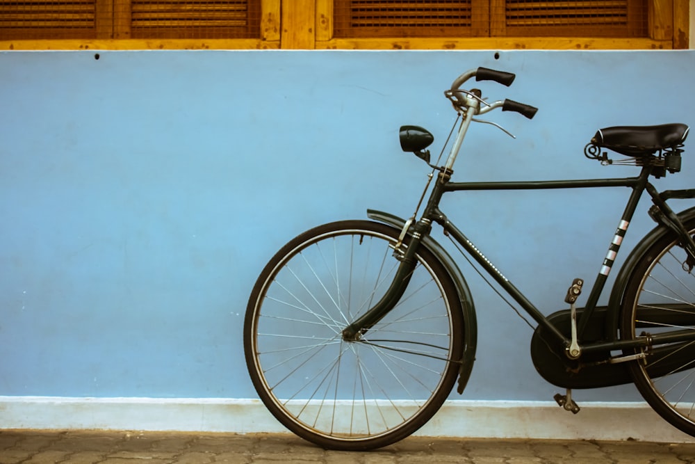 a black bicycle leaning against a blue wall