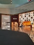 A shopping mall interior featuring high-end luxury fashion stores. The storefronts include Celine, Loro Piana, and Gucci. The design is modern with an illuminated ceiling and glossy floors reflecting the ambient lighting. Display windows showcase fashion items, and the space appears spacious and well-organized.