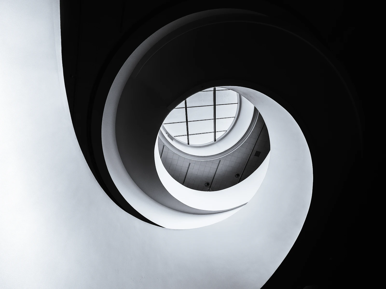 A spiral staircase seen from below, rising toward a skylight