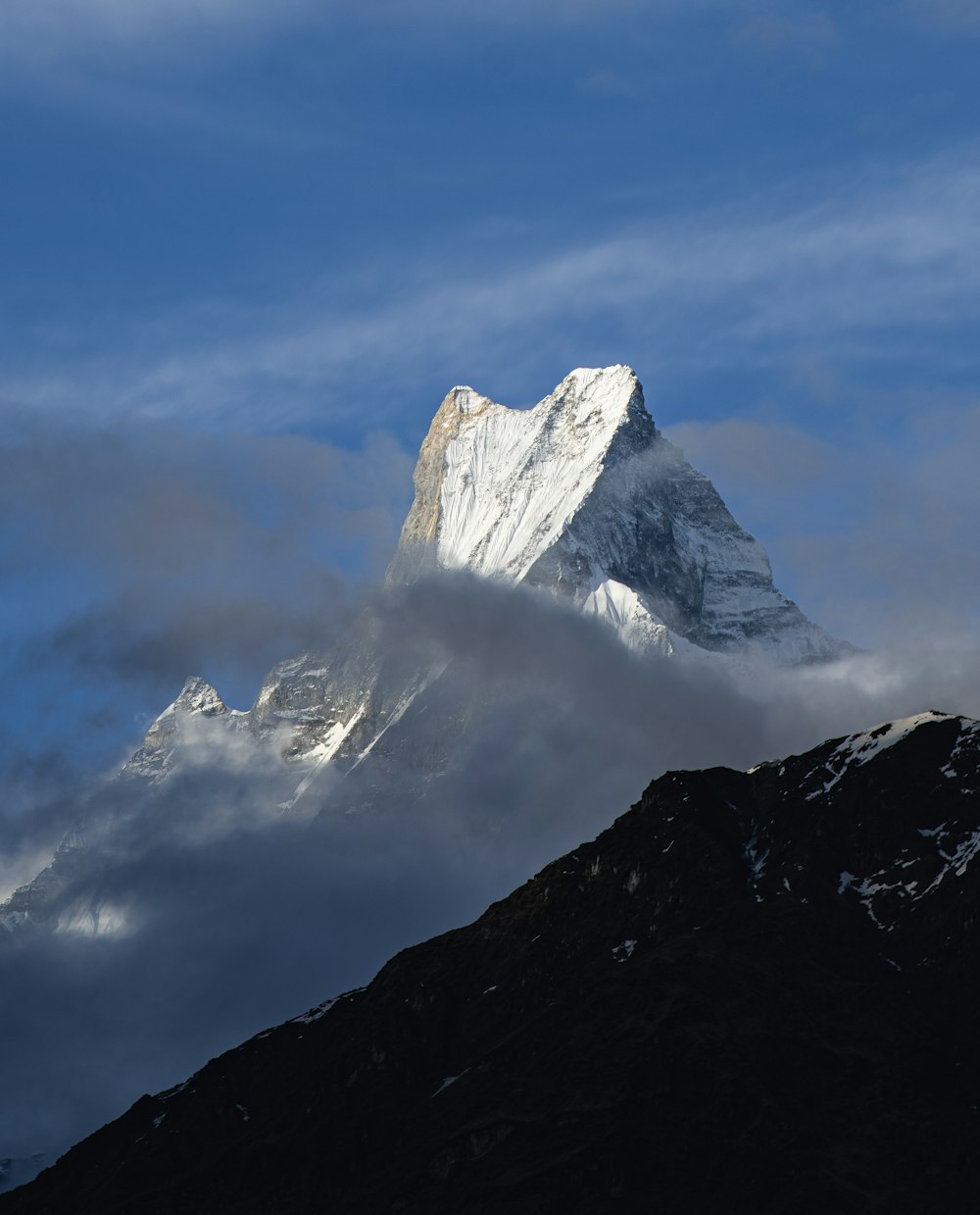 a large mountain covered in clouds under a blue sky