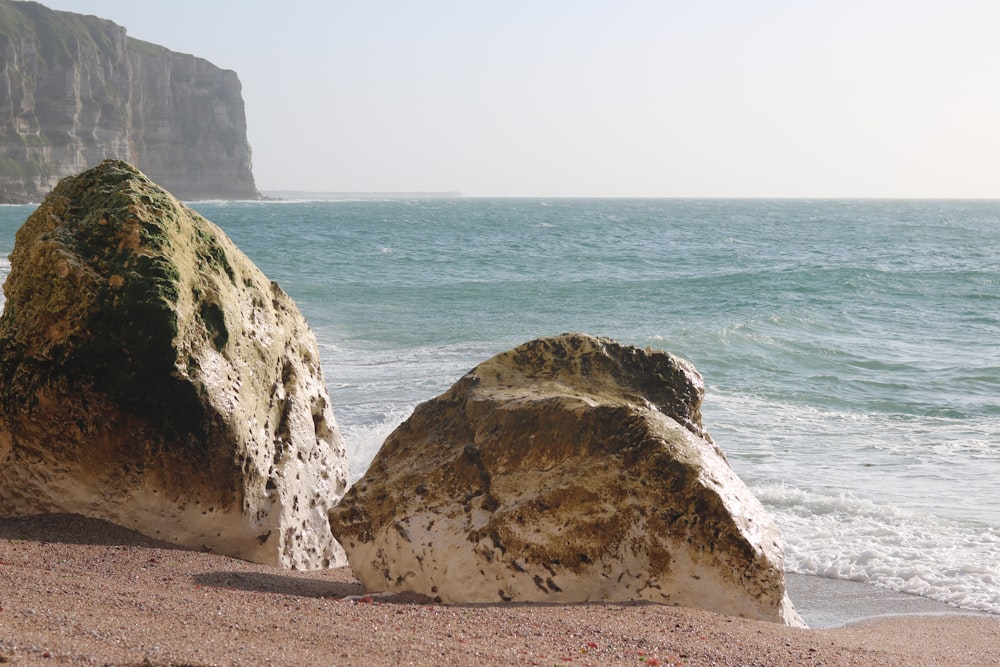 two large rocks sitting on top of a sandy beach