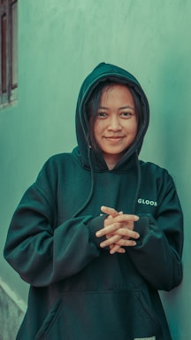 a woman wearing a green hoodie standing in front of a blue wall