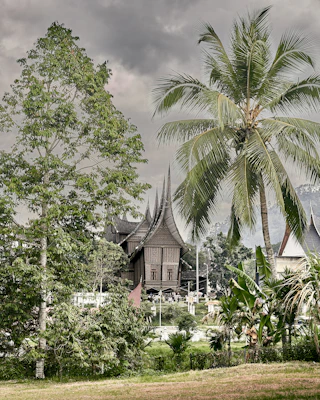 A vibrant photo of a traditional Minangkabau house with its distinctive curved roof under a bright blue sky.