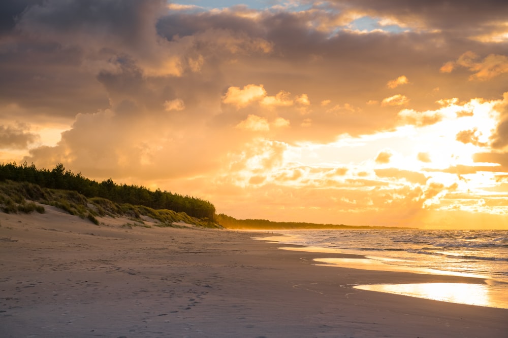 the sun is setting on the beach with footprints in the sand