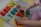 A child is playing with a colorful wooden puzzle board featuring numbers and geometric shapes. The numbers range from 1 to 9 in various bright colors like red, orange, yellow, and green. Next to the numbers, there are rainbow-colored semicircles arranged on a wooden base. The child's hands are interacting with the puzzle pieces, and the child is wearing a purple outfit with white polka dots on a textured play mat.