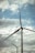 Several wind turbines with large blades are seen against the backdrop of a cloudy sky. Power lines also run horizontally across the image, contributing to the industrial feel.
