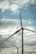 Several wind turbines with large blades are seen against the backdrop of a cloudy sky. Power lines also run horizontally across the image, contributing to the industrial feel.