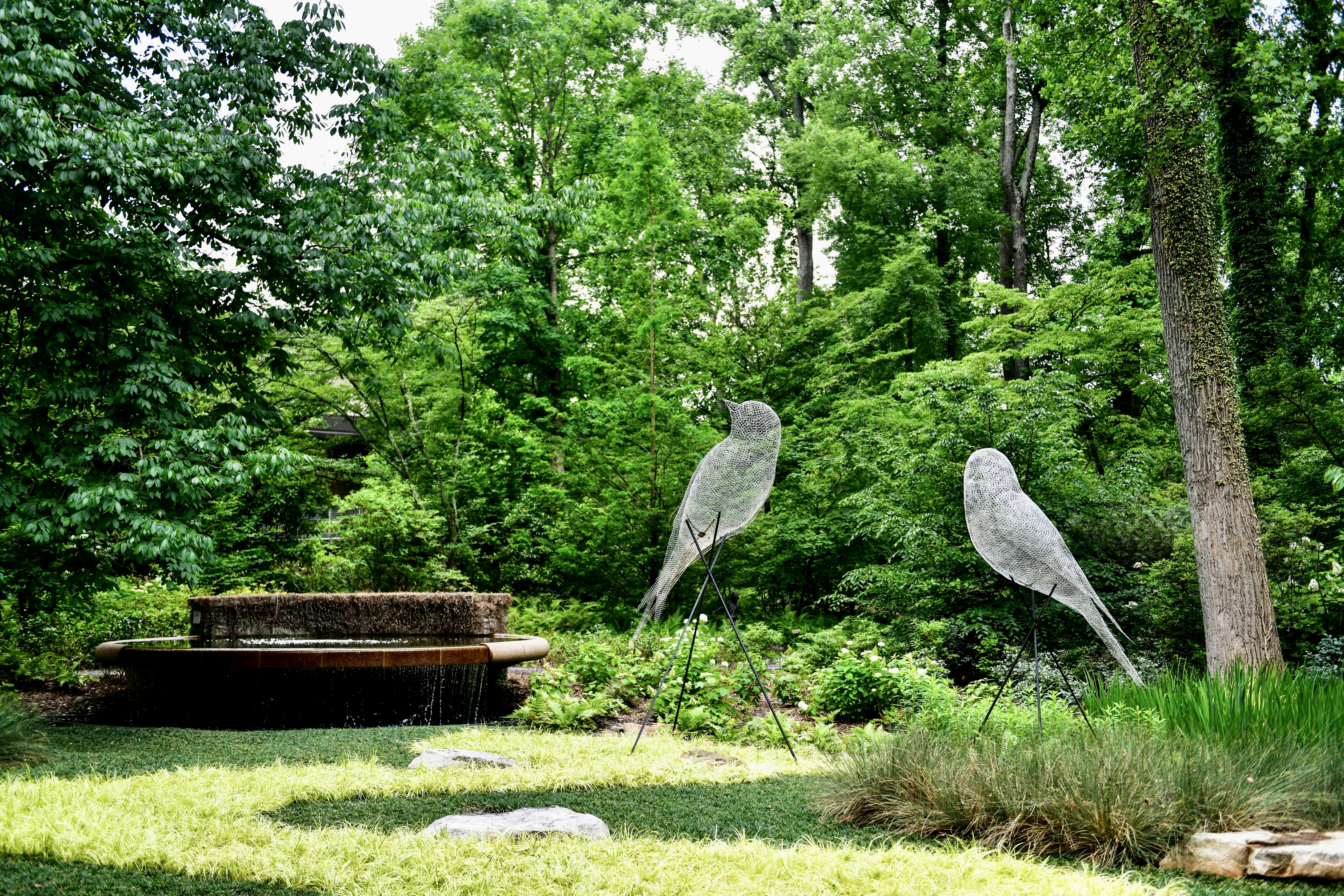a couple of metal birds sitting on top of a lush green field