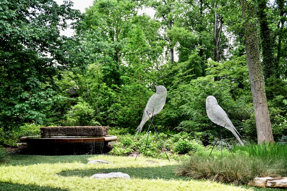 a couple of metal birds sitting on top of a lush green field