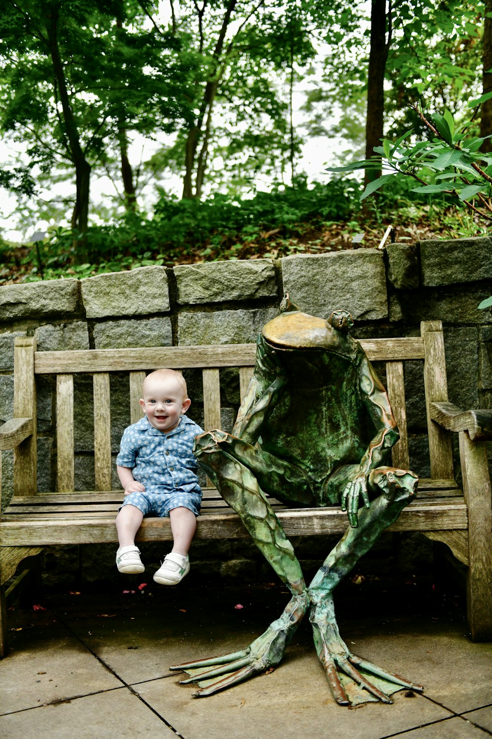 a baby sitting on a bench next to a statue of a frog