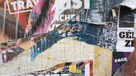A collage of torn and overlapping posters featuring various colors, fonts, and partial text fragments. The layers reveal bits of images and words such as 'TRAV', 'STREET', and others, creating a textured and chaotic visual effect.