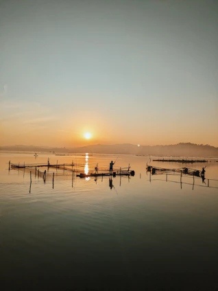 A serene sunrise over a calm sea with drones surveying fishing boats in the distance.