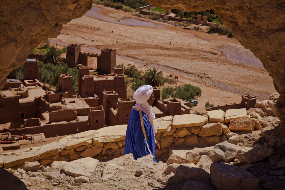 a woman in a blue dress standing in front of a desert village