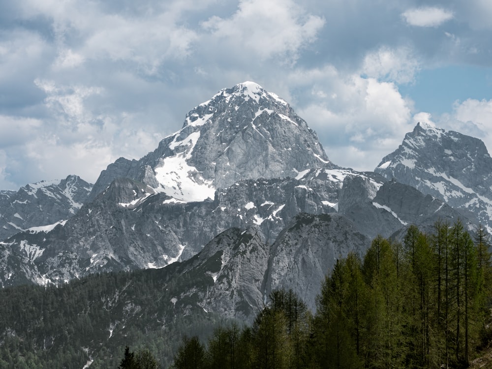 a mountain range with trees in the foreground and clouds in the background