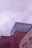A building structure featuring a combination of brick and metal surfaces. The lower portion shows a red brick wall, while the upper section is made of weathered, corrugated metal with a bluish hue. The sky above is overcast with a soft, cloudy texture.
