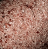 A close-up view of coarse pink salt crystals, varying in size and texture, with a subtle shimmer effect.