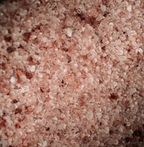 A close-up of pink Himalayan salt crystals spilling from a rustic wooden scoop.