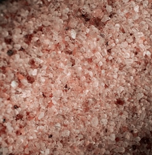 A close-up view of coarse pink salt crystals, varying in size and texture, with a subtle shimmer effect.