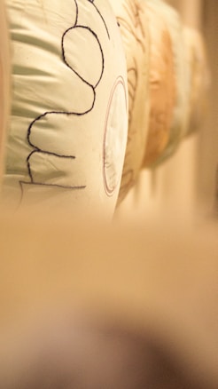 A close-up view of a row of wheels or barrels. The surface is covered with light fabric, and some stitching or text is visible. The background appears blurred, giving a focus on the nearest object.
