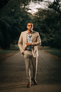 A confident man dressed in a tailored beige blazer and crisp white shirt, walking in an urban setting.