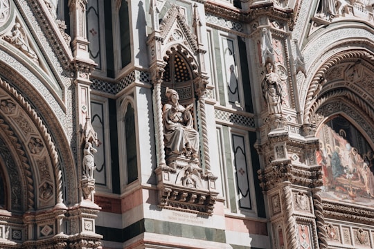 An ornate architectural facade featuring intricate sculptures and detailed stone carvings. The design includes statues of figures set in alcoves, elaborate patterns, and colorful mosaic work. The craftsmanship is highly detailed, reflecting historical and artistic elements.