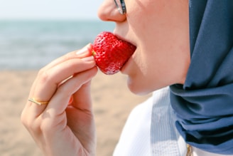 a woman eating a strawberry on the beach