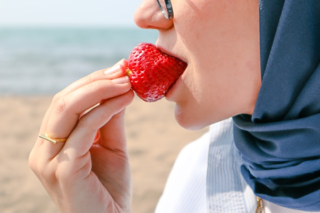 a woman eating a strawberry on the beach