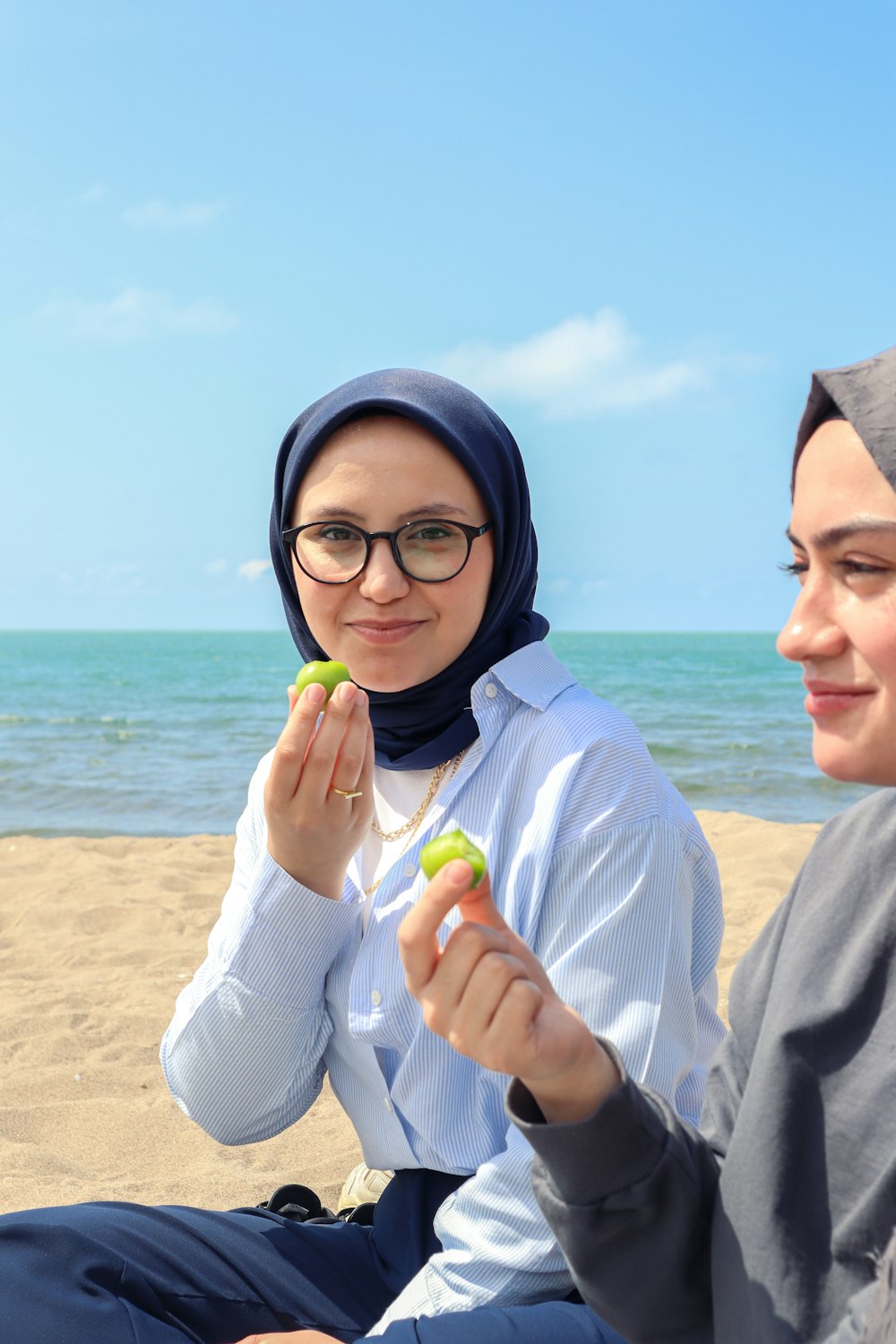 two women sitting on a beach holding green objects