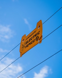 a yellow danger electric fence sign hanging from a wire