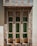 Three narrow rectangular windows, each with decorative green stained glass panels, are set in a stone facade featuring a variety of beige, brown, and gray stones. The facade has a geometric pattern, adding a textured and rustic look to the building exterior.