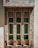 Three narrow rectangular windows, each with decorative green stained glass panels, are set in a stone facade featuring a variety of beige, brown, and gray stones. The facade has a geometric pattern, adding a textured and rustic look to the building exterior.