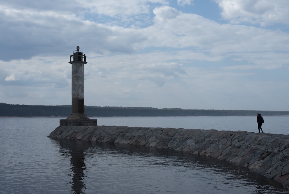 a person standing on the edge of a body of water next to a light house