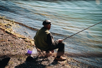 a man sitting on the shore of a lake fishing