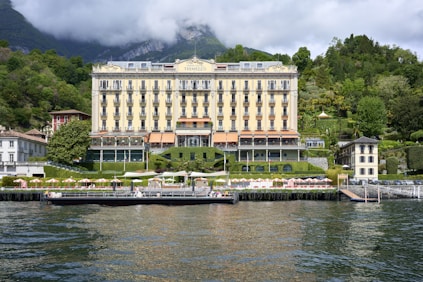 a large building sitting on top of a lake next to a lush green hillside