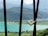 A padlock is attached to black metal bars overlooking a serene landscape featuring a turquoise lake, greenery, and distant mountains under a partly cloudy sky.