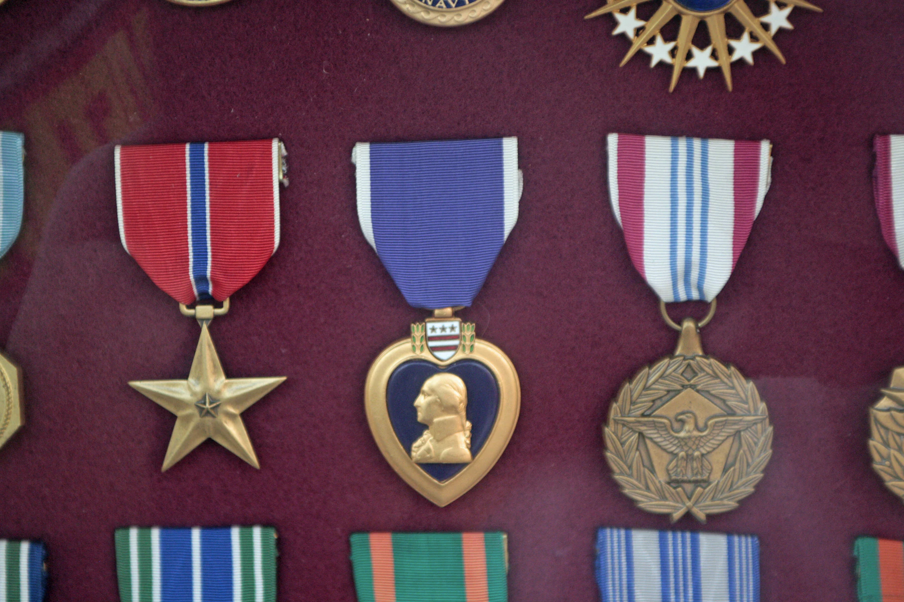 A bronze star, a purple heart and other medals mounted on maroon cloth in a display case