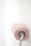 A paint roller covered in pink paint is pressing against a white wall. The roller appears to be in mid-action, with the paint on the roller appearing thick and textured.