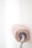 A paint roller covered in pink paint is pressing against a white wall. The roller appears to be in mid-action, with the paint on the roller appearing thick and textured.