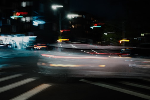 Nighttime city street with glowing car lights and motion blur.